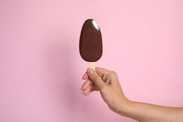 Wall Mural - Woman holding bitten ice cream glazed in chocolate on pink background, closeup
