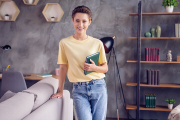 Poster - Photo of pretty charming young lady wear yellow t-shirt smiling holding book indoors room home