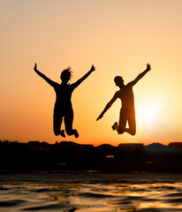 Happy friends are having fun and jump at sunset beach in sunlight