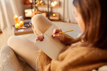 Wall Mural - halloween, holidays and leisure concept - young woman with pencil writing to diary at cozy home