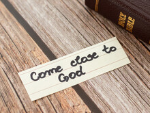 Come Close To God Jesus Christ. A Closeup Of A Handwritten Quote And Closed Holy Bible Book On Wooden Background. Repentance, Humility, Belief, Trust In The LORD. Christian Biblical Concept.