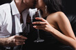 cropped view of blurred and sexy couple holding glasses of red wine while kissing isolated on black.