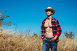 Handsome young man with a perfect body posing in cowboy hat, plaid shirt and jeans in the field. Outdoor shot.