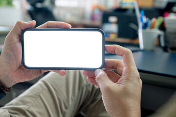 Wall Mural - cropped shot of man hand holding blank white screen smartphone in horizontal view while sitting at o