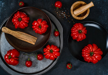 Wall Mural - Ripe red tomatoes lie on a black plate on a black background with wooden dishes, top view.