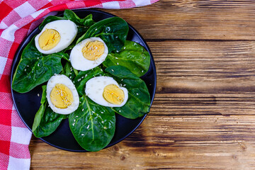 Wall Mural - Spinach leaves and halved boiled eggs on a black plate. Top view