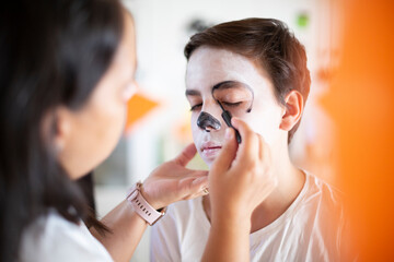 Close up of woman putting makeup on teenage boy for Day of the Dead celebration. (Dia de los Muertos).