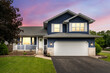 © Joe Hendrickson - Exterior of a suburban home with blue siding, a white front porch, and white shutters at sunset.