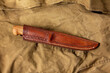 A knife with a fixed blade in a leather sheath with a pattern on a brown canvas. Traditional scandinavian knife