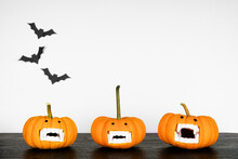 Fun Halloween Pumpkins With Vampire Teeth On A Black Shelf Against A White Wall With Bats. Copy Space.