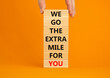 Go the extra mile symbol. Wooden blocks with words 'We go the extra mile for you'. Businessman hand. Beautiful orange background. Business and go the extra mile concept. Copy space.