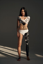 Full Length View Of The Tattooed Female With Cyborg Pattern On Her Body Posing At The Studio On Dark Background. People And Robot Concept