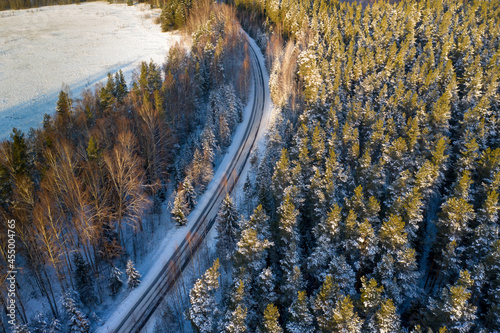 Auto track in winter forest. Northern nature with road. Winter track from bird\'s eye view. Winter taiga with empty highway. Snowy taiga. Coniferous trees next to automobile highway. Auto travel route