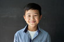 Happy Cute Asian Kid Boy School Student Looking At Camera At Blackboard Background. Smiling Ethnic Child Pupil Posing In Classroom. Junior Elementary Education. Back To School In Asia Concept Portrait