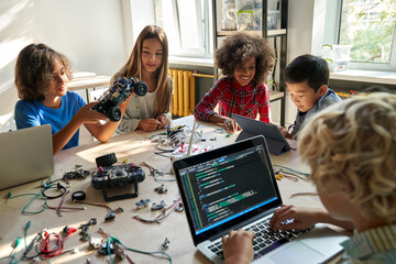 diverse school children students build robotic cars using computers and coding. happy multiethnic ki