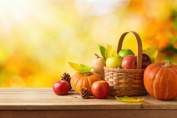 Wall Mural - Thanksgiving holiday and autumn season concept with pumpkin, apples and fall leaves in basket on wooden table over autumn bokeh background