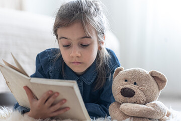 Wall Mural - Little girl reads a book with a teddy bear.