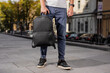 A black leather backpack holding male hand in city