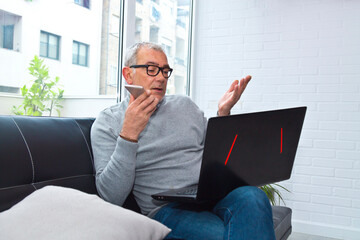 Wall Mural - mature man using laptop while talking on the phone at home or workplace