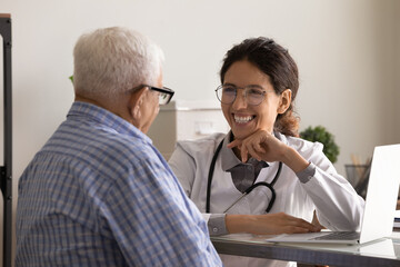 Wall Mural - Happy friendly GP doctor meeting with senior 80s male patient, talking to old man, laughing at joke. Young therapist giving consultation, medical treatment advice at appointment. Elderly healthcare