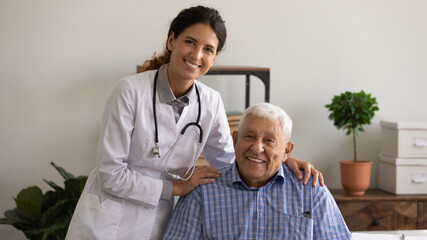 Wall Mural - Head shot portrait of optimistic young female therapist and happy older patient. Senior man visiting doctor, looking at camera, smiling, staying healthy due to good treatment, geriatric medic care