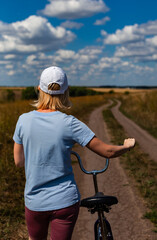 woman with a bicycle on the background of a rural road stretching into the distance