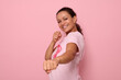 © Taras Grebinets - Pretty woman in pink t-shirt and cancer awareness ribbon stands in fighting stance to mark the fight against cancer, in honor of October 1st , smiles looking at camera, colored background, copy space