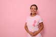 © Taras Grebinets - Smiling mixed race woman in pink T-shirt with pink satin ribbon symbolizing International Breast Cancer Day, expressing solidarity and support for breast cancer patients and survivors. 1 st october