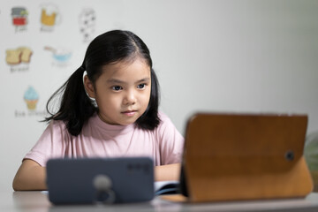 Wall Mural - Asian child student or kid girl smiling learn from home school or people study online on computer tablet and video call learning on smartphone with happy enjoy to vocabulary english words in classroom