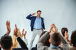 © dusanpetkovic1 - Smiling motivational speaker standing in front of his audience who is clapping.