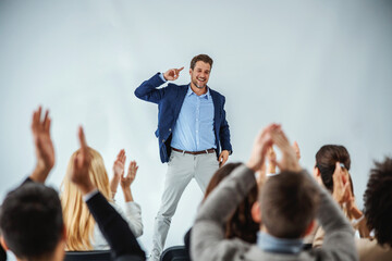 smiling motivational speaker standing in front of his audience who is clapping.