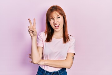 Sticker - Redhead young woman wearing casual pink t shirt smiling with happy face winking at the camera doing victory sign. number two.