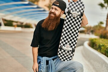 Wall Mural - Young irish skater man smiling happy holding skate at the city.