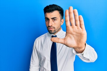 Wall Mural - Young hispanic man wearing business clothes doing stop sing with palm of the hand. warning expression with negative and serious gesture on the face.