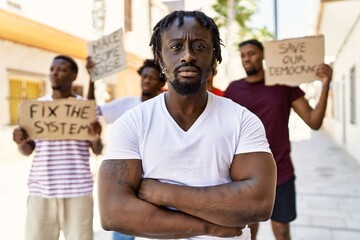 Wall Mural - Young activist man with arms crossed gesture standing with a group of protesters holding banner protesting at the city.