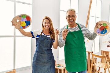 Wall Mural - Two middle age artists smiling happy holding paintbrushes and palette at art studio.