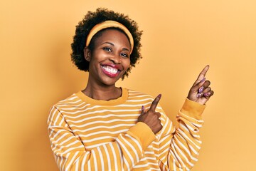 Young african american woman wearing casual sweatshirt smiling and looking at the camera pointing with two hands and fingers to the side.