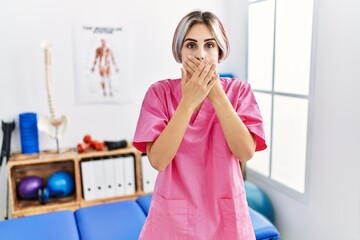 Sticker - Young nurse woman working at pain recovery clinic shocked covering mouth with hands for mistake. secret concept.