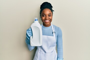 Poster - African american woman with braided hair holding detergent bottle looking positive and happy standing and smiling with a confident smile showing teeth