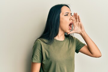 Young hispanic girl wearing casual t shirt shouting and screaming loud to side with hand on mouth. communication concept.