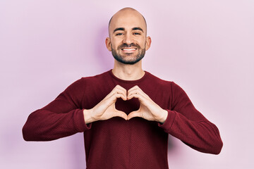 Canvas Print - Young bald man doing heart symbol with hands smiling with a happy and cool smile on face. showing teeth.