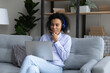 © fizkes - Pensive afro american teen female learn on distance sit on sofa wear headset hold laptop on knees prepare for test exam. Concentrated young black lady student listen to video record of lecture on pc