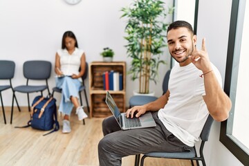 Young people sitting at waiting room working with laptop surprised with an idea or question pointing finger with happy face, number one