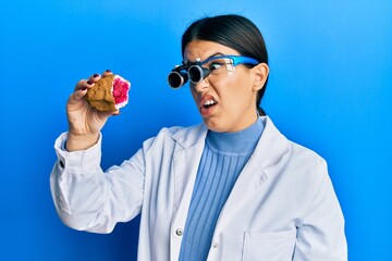 Canvas Print - Beautiful brunette jeweller woman holding geode stone wearing magnifier glasses clueless and confused expression. doubt concept.