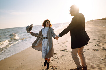 Wall Mural - Young couple having fun walking and hugging on beach during autumn sunny day. Relaxation, youth, love,  lifestyle solitude with nature.