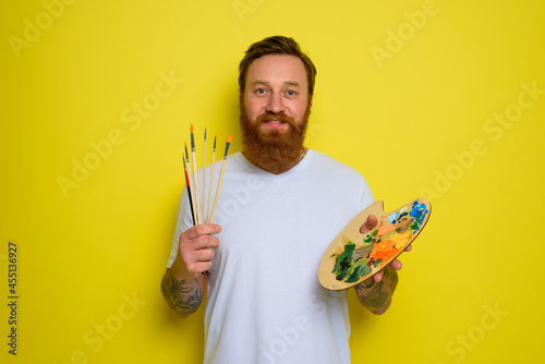 Happy man with beard and tattoo is ready to draw with brushes