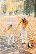 © Валентина Свиридо - mom in a knitted hat gently looks at her daughter of five years old holding her hand in the fall against the background of fallen yellow leaves, next to their pet a small dog