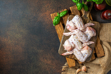 Wall Mural - Raw chicken wings on a wooden board on a dark culinary background top view from a copyspace. The process of cooking poultry	
