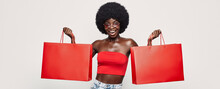 Beautiful Young African Woman Carrying Red Shopping Bags And Smiling While Standing Against Gray Background