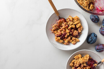 Wall Mural - Plum crumble dessert in plates with spoons on white background for tasty breakfast. Top view